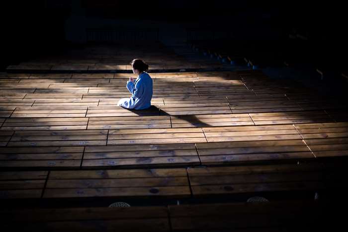 Woman sitting alone on wooden floor in sunlight