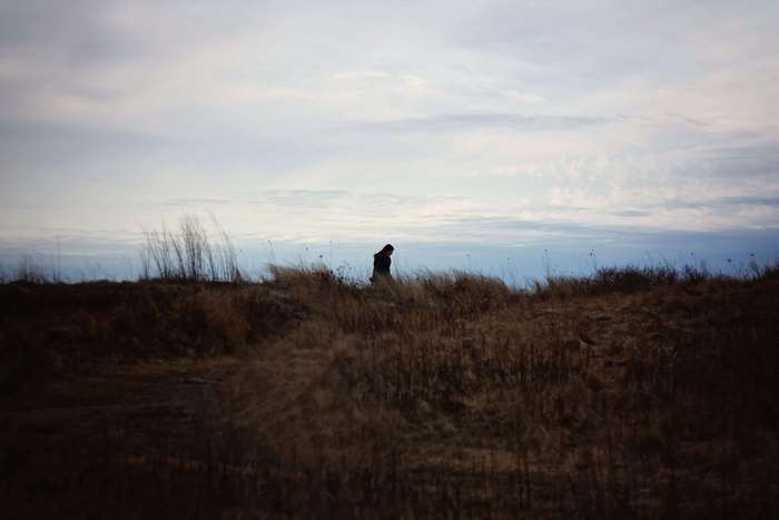 Woman walking on a grassy hill with cloudy sky