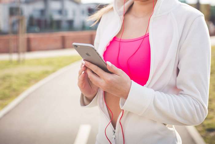 Woman in pink sports bra and white jacket using iPhone