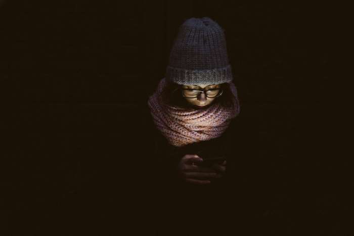 Woman wearing a hat and scarf using a mobile phone in the dark