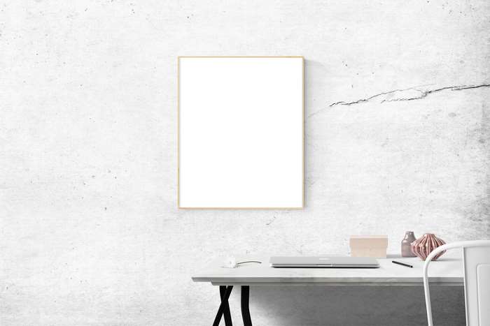 Blank picture frame mockup above a desk with laptop