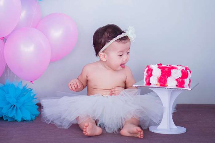 Baby girl in tutu with birthday cake and balloons