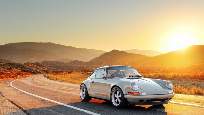 Porsche 911 driving on a desert road at sunset