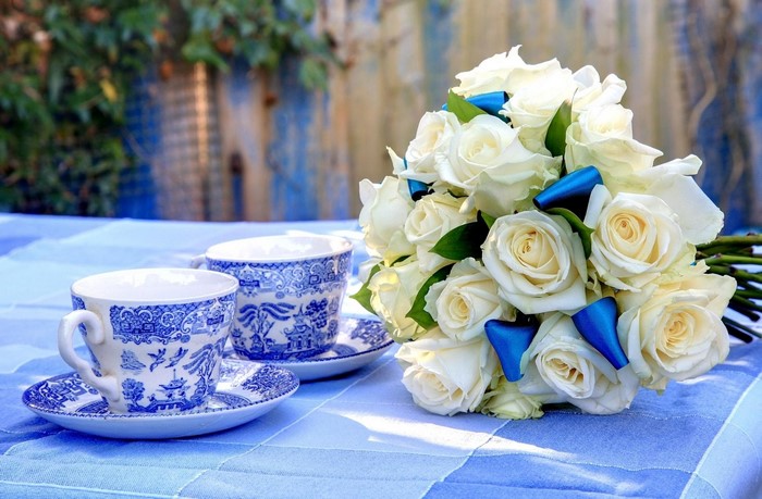 White roses with blue ribbons and tea cups on a table