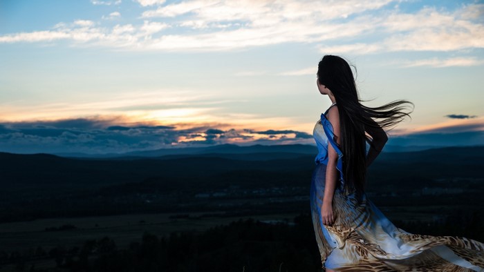 Woman in flowing dress on a hill at sunset
