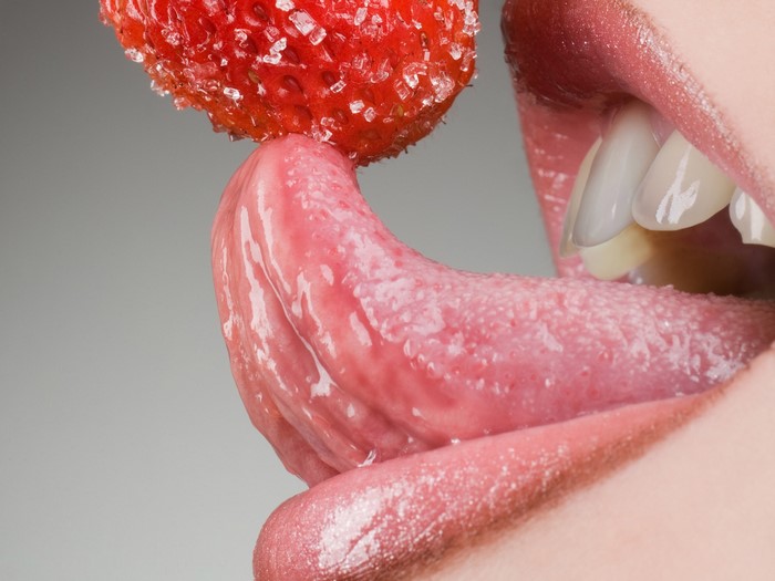 Close-up of a tongue licking a sugar-coated strawberry