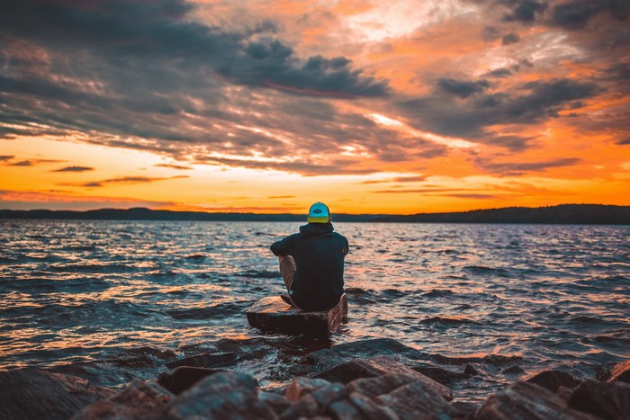 Man sitting on rocks by the sea at sunset