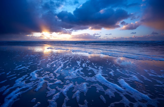 Sunset over the ocean with waves and foam on the beach