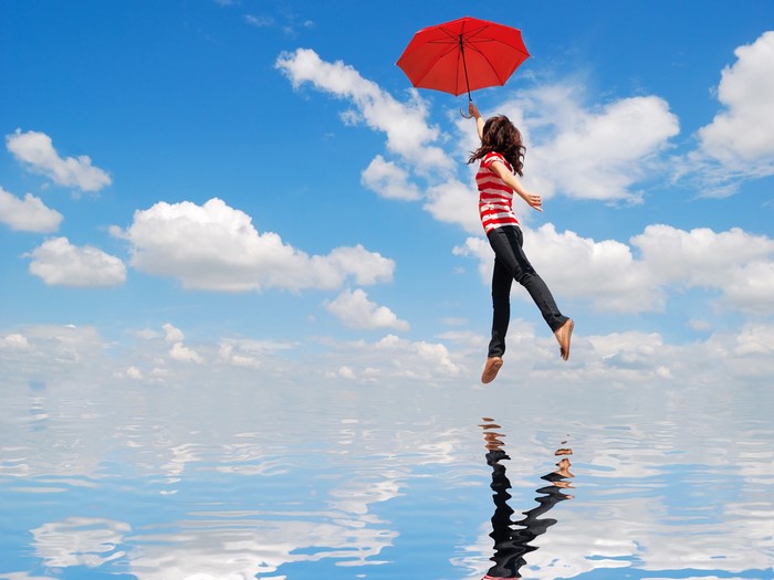 Girl flying with red umbrella over water