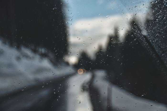 Raindrops on a car window overlooking a snowy road