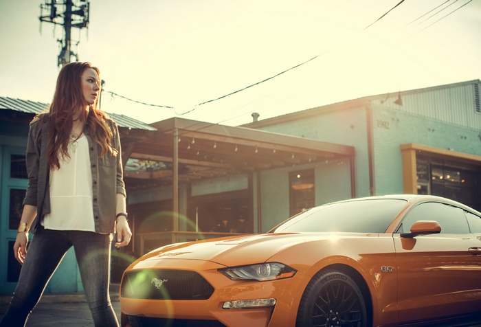 Woman standing next to an orange Ford Mustang