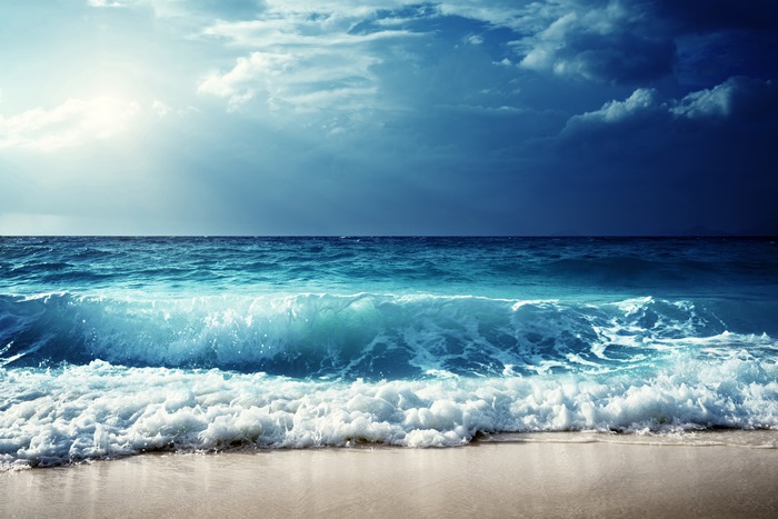 Ocean waves crashing on a sandy beach under a cloudy sky