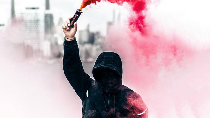 Person in hoodie holding red smoke grenade