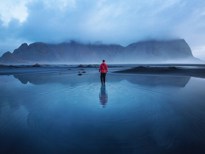 Man walking on a wet beach with mountains in the background