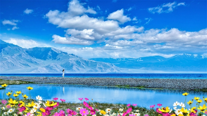Woman walking by a lake with mountains and flowers