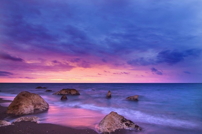 Sunset over a rocky beach with purple and pink clouds