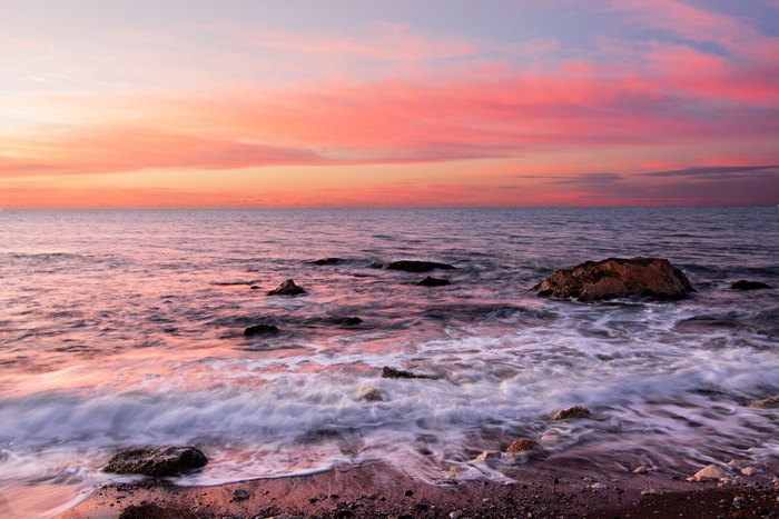 Sunset over the ocean with pink clouds and rocks