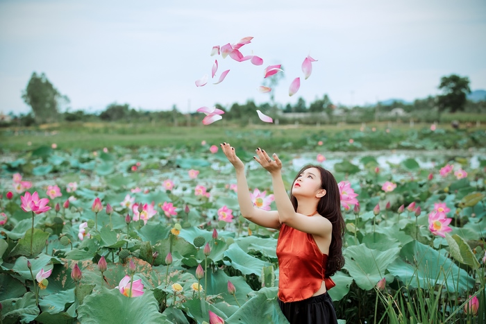 Woman in a lotus field throwing petals