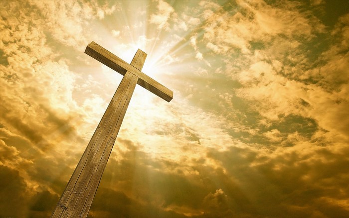 Wooden cross against a cloudy sky with sunbeams