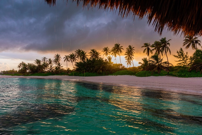 Tropical beach with palm trees during a rain shower at sunset