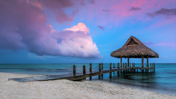 Wooden pier with thatched hut at sunset over the ocean