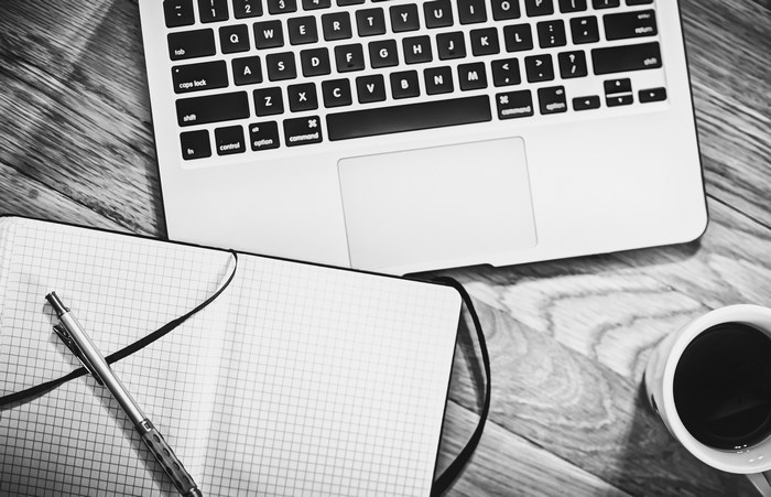 Laptop, notebook, pen, and coffee on a wooden desk