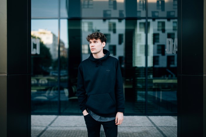 Young man in black hoodie standing in front of modern building