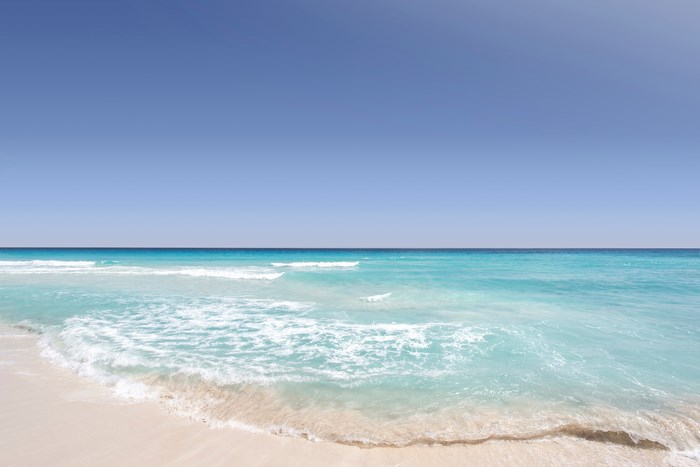 Turquoise ocean waves on a sandy beach under a clear blue sky