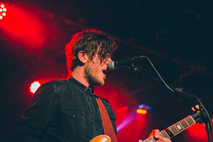 Male guitarist singing into microphone on stage