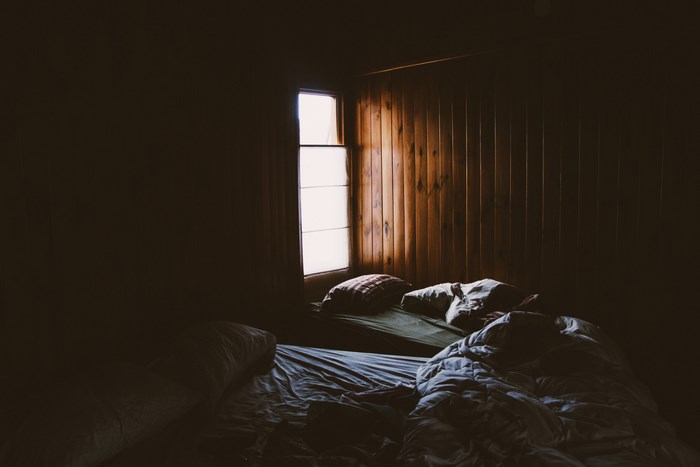 Messy bed in a cabin with wood walls and sunlight