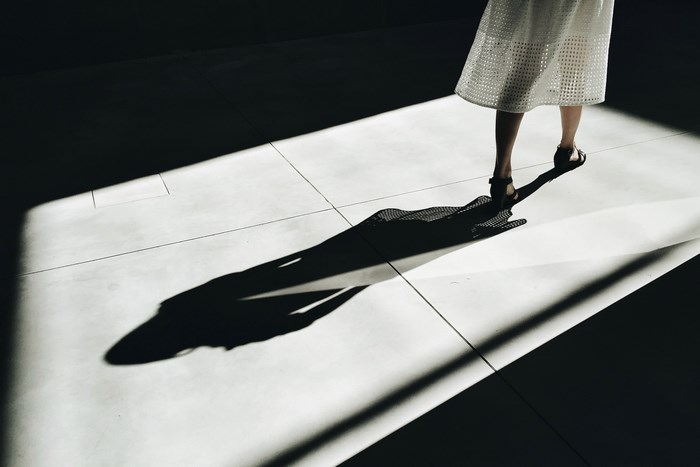 Woman in white skirt and sandals casting a long shadow