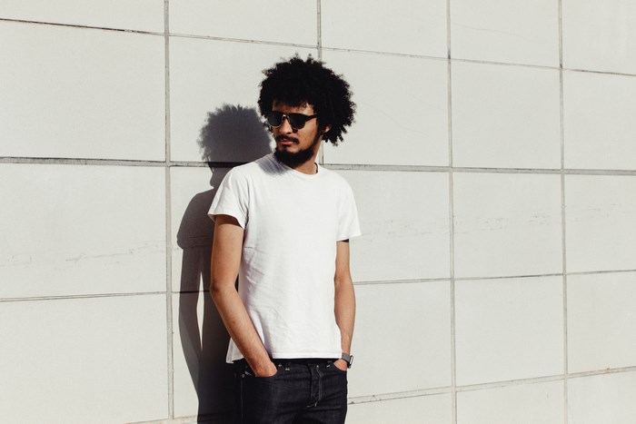 Man with afro and sunglasses standing against a tiled wall