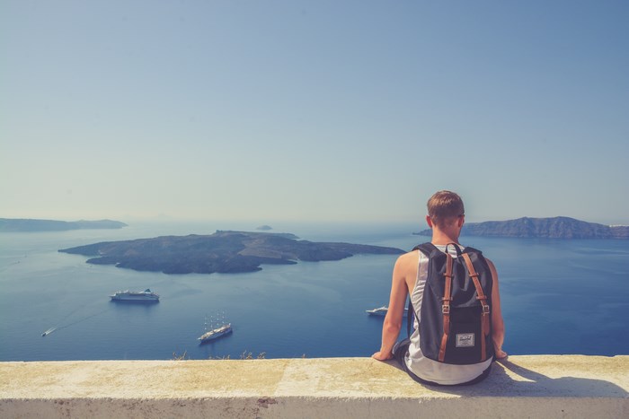 Man with backpack sitting on edge overlooking ocean islands