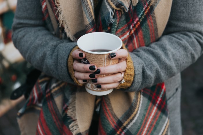 Cozy hands holding warm drink with plaid scarf