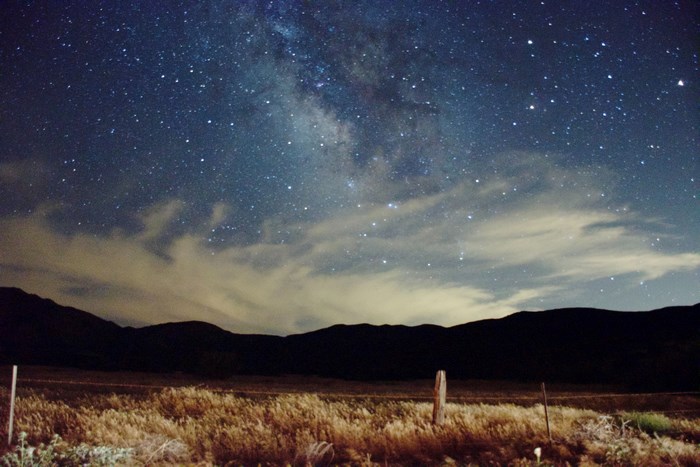 Milky Way galaxy over a dark mountain range and meadow