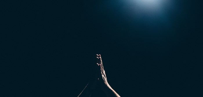 Hands in prayer gesture with light from above