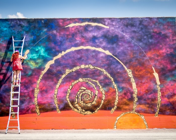 Artist painting a colorful spiral mural on a wall