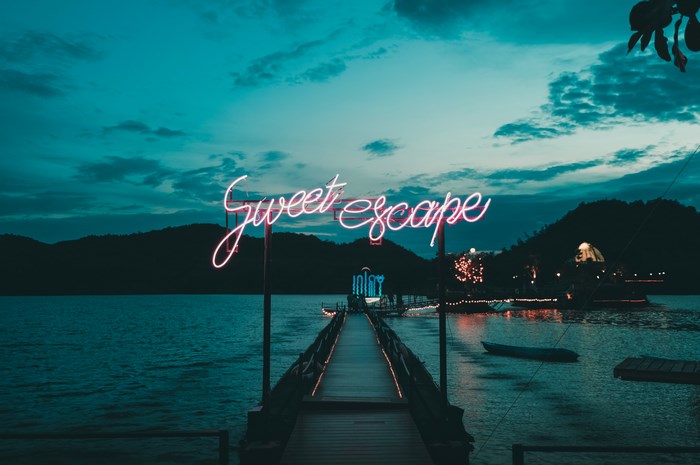Neon 'Sweet Escape' sign over a pier at dusk