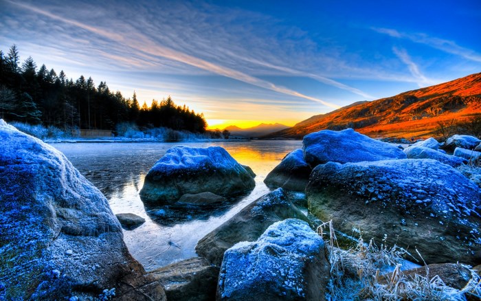 Frozen lake with rocks and sunset over mountains