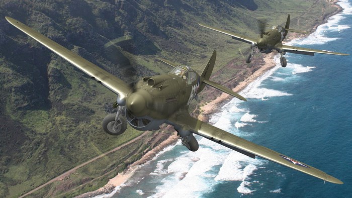 Two Curtiss P-40 Warhawk airplanes flying over a coastline