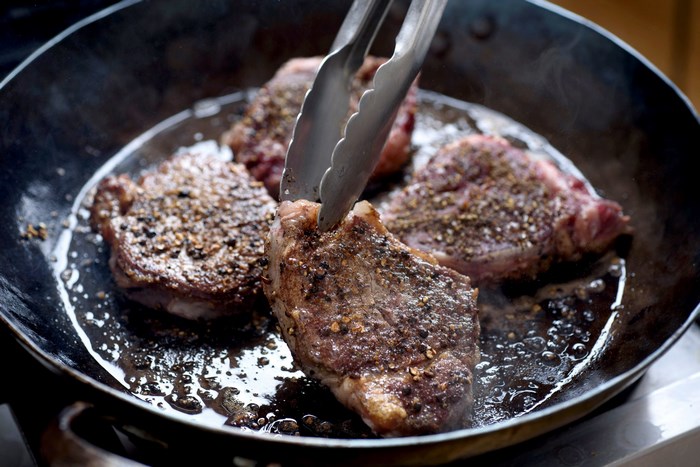 Steaks being seared in a cast iron pan