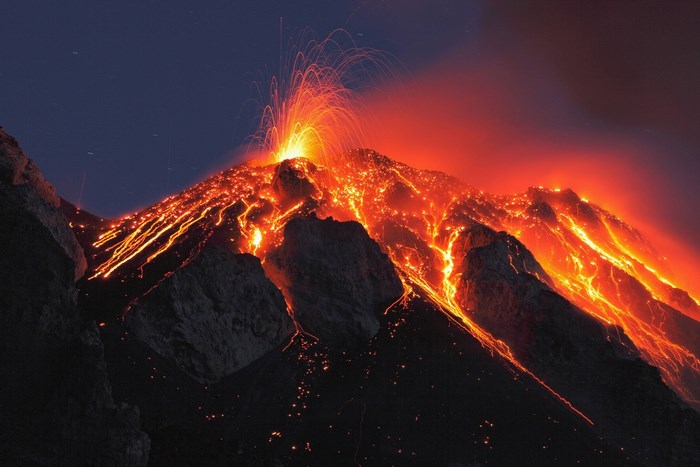 Volcano erupting with lava flows at night