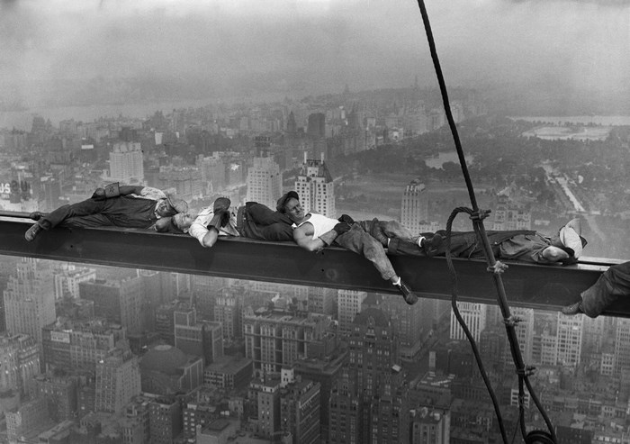 Construction workers resting on a steel beam high above New York City