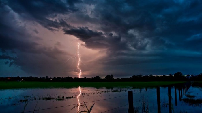 Lightning strikes over a flooded field at dusk