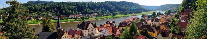 Panoramic view of a riverside town with forested hills