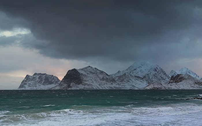 Snowy Mountains Overlooking a Choppy Sea Under Dark Clouds