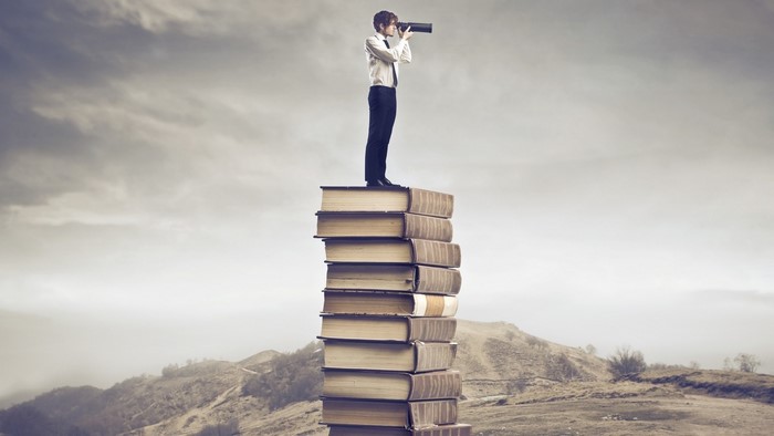 Man with telescope on stack of books
