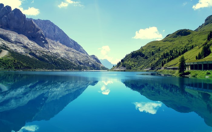 Lake reflecting mountains and green hills under a blue sky