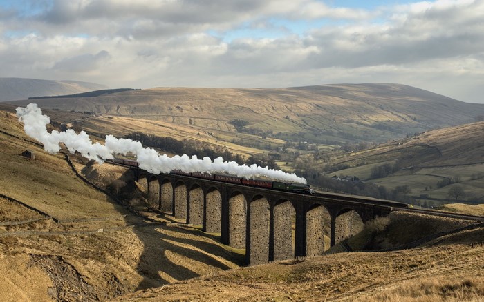 Steam train on a stone viaduct in a hilly landscape