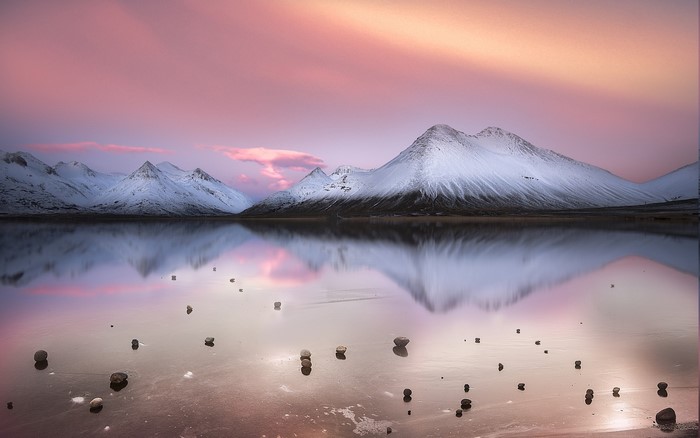 Snowy mountains reflected in a calm lake at sunset